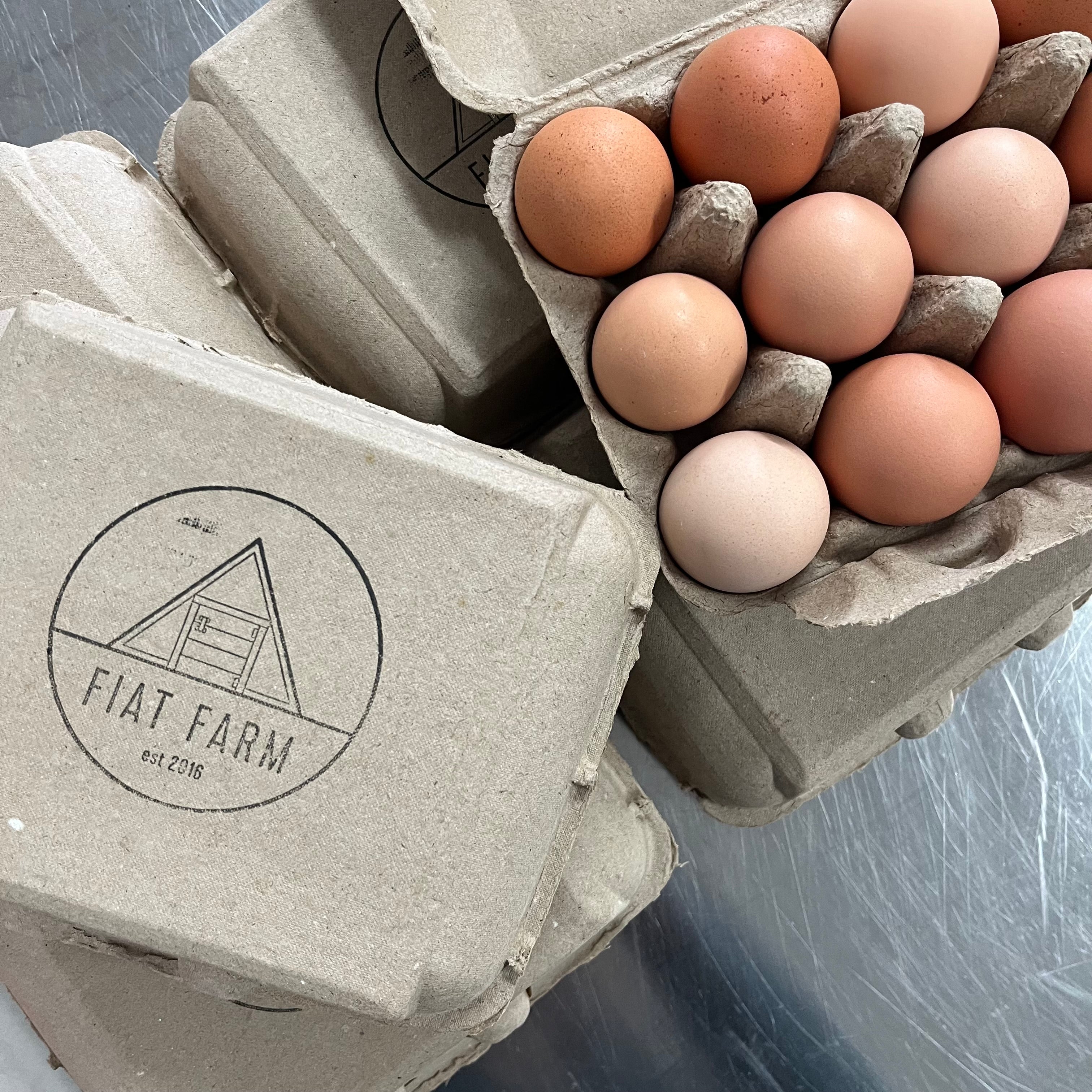 Eggs in a cardboard carton with 'Fiat Farm' branding on a metallic surface